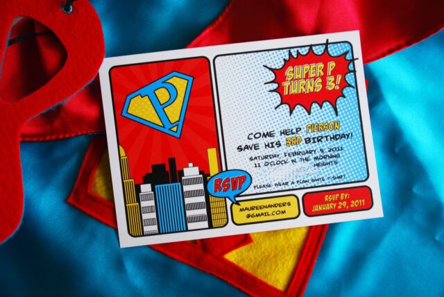 Vintage pop art Super Hero birthday party dessert table with comic book decorations, colorful city skyline backdrop, superhero cake, cupcakes, and candy bar.