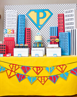 Vintage pop art Super Hero birthday party dessert table with comic book decorations, colorful city skyline backdrop, superhero cake, cupcakes, and candy bar.