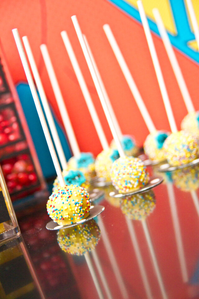 Vintage pop art Super Hero birthday party dessert table with comic book decorations, colorful city skyline backdrop, superhero cake, cupcakes, and candy bar.