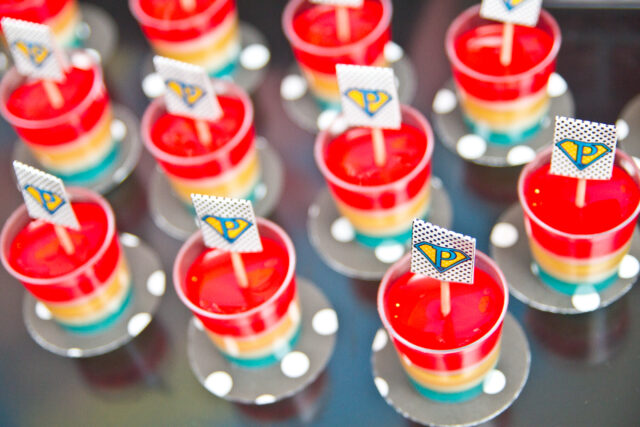 Vintage pop art Super Hero birthday party dessert table with comic book decorations, colorful city skyline backdrop, superhero cake, cupcakes, and candy bar.
