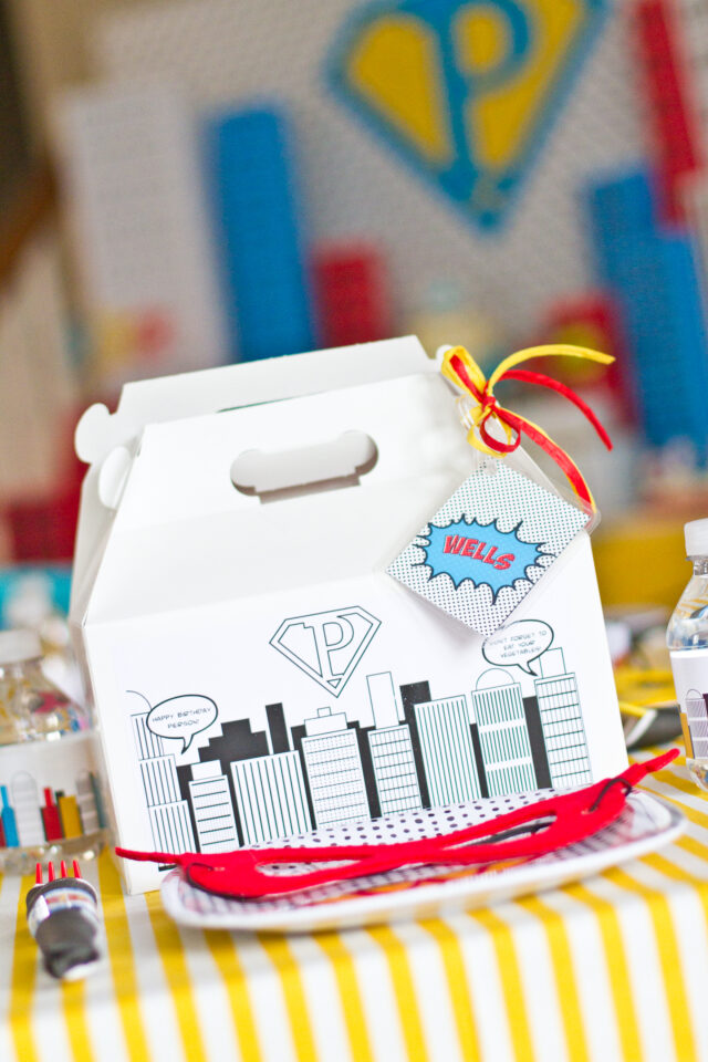 Vintage pop art Super Hero birthday party dessert table with comic book decorations, colorful city skyline backdrop, superhero cake, cupcakes, and candy bar.