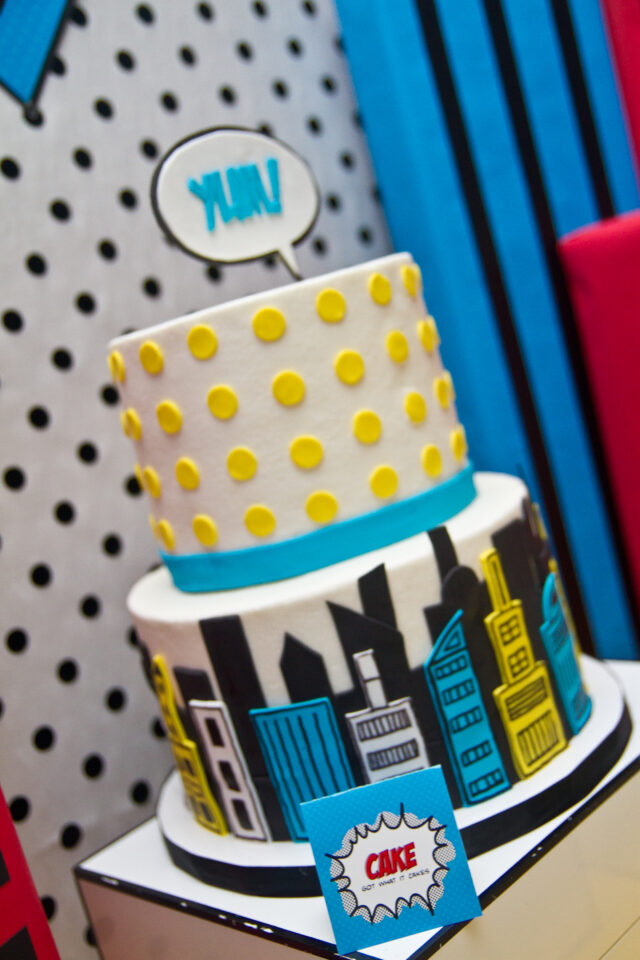 A colorful vintage pop art inspired Super Hero birthday party featuring comic book graphics, bold city skyline decorations, superhero desserts, candy displays, DIY activities, capes, masks, and interactive party games for kids.