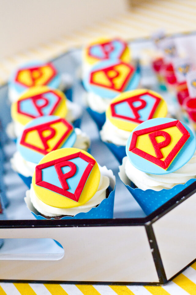 Vintage pop art Super Hero birthday party dessert table with comic book decorations, colorful city skyline backdrop, superhero cake, cupcakes, and candy bar.